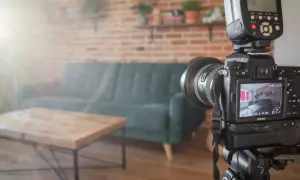 Aparat fotograficzny na statywie w salonie, gotowy do ujęć. W tle kanapa i ceglana ściana, tworzące atmosferę do trików z dymu.