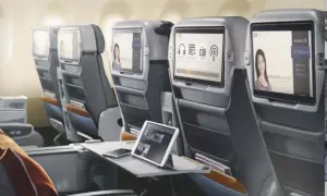 Komfortowe fotele w klasie lot premium economy. Ekrany rozrywki pokładowej, tablet i telefon na stoliku.