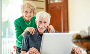 Couple souriant devant un ordinateur, discutant de l'obligation alimentaire en EHPAD et des impôts.