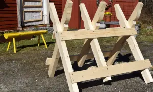 En nybyggd sågbock ritning i trä, redo för vedhuggning. En gul bänk syns i bakgrunden.