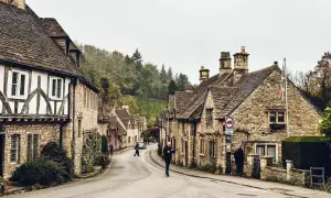 Kamienna uliczka w Cotswolds, z tradycyjnymi domami i drzewami na wzgórzach.