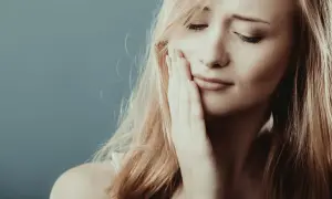 Kobieta z opuchniętym policzkiem, dotyka go dłonią, wyrażając dyskomfort, choć nie widać bólu zęba.