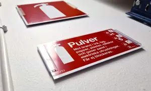 Röd skylt för pulverbrandsläckare, klassad brandklass A1. Informerar om att den släcker bränder i trä, tyg, papper, vätskor och gaser.