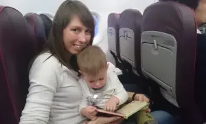Mama z dzieckiem w samolocie Wizzair. Dziecko przegląda książeczkę, siedząc na kolanach mamy.