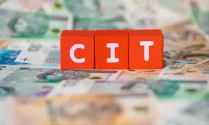 Trzy pomarańczowe klocki z literami "C", "I", "T" leżą na tle polskich banknotów. Podatek CIT to ważna część finansów.