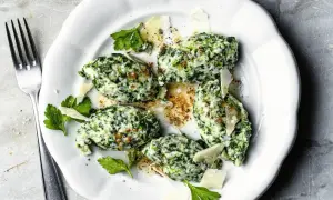 Malfatti Rezept: Grüne Klößchen aus Spinat und Ricotta, garniert mit Parmesan und Petersilie, auf einem weißen Teller.