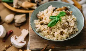 Aksamitne **ryże** z grzybami, udekorowane listkiem bazylii, na drewnianej desce. Obok świeże grzyby i papryczka chili.