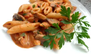 Penne z kremowym sosem pomidorowym i pieczarkami, udekorowane natką pietruszki. Pyszny makaron z pieczarkami.