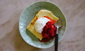 En bit ostkaka med keso, toppad med grädde och jordgubbar, på en mintgrön tallrik med en gaffel.