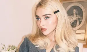 Blondynka w szarym żakiecie, z błyszczącą cerą i mocno podkreślonymi oczami, prezentuje styl makijaż lata 2000.