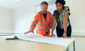 Inżynier w kamizelce odblaskowej omawia plany z klientką, przygotowując odbiory mieszkań od dewelopera.