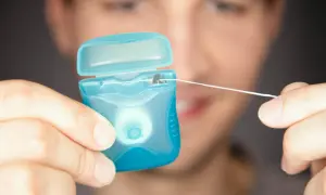 Mężczyzna przygotowuje się do nitkowania zębów, trzymając w dłoniach niebieskie opakowanie z nicią dentystyczną.