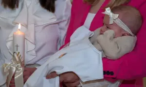 Chrzestny bez bierzmowania wyjątki. Niemowlę w białej szatce, trzymane przez kobietę w różowej marynarce, obok płonąca świeca.