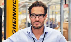 Georgi Ganev, med glasögon och ljusblå skjorta, står framför en gul gaffeltruck i ett lager.