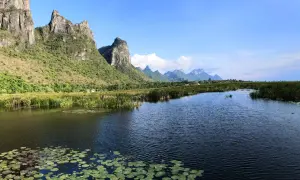 Khao Sam Roi Yot National Park: Majestätische Berge ragen über einen ruhigen Fluss mit Seerosen und Schilf auf.