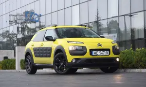 Żółty Citroen C3 Cactus z czarnymi felgami i charakterystycznymi panelami Airbump stoi przed nowoczesnym budynkiem.