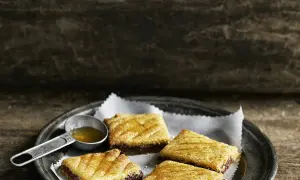 Quatre makrouts algériens sur une assiette, arrosés de miel. Une cuillère doseuse remplie de miel est à côté. Parfait pour une recette makrout algérien facile.