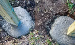 Holzpfosten werden in frischen Beton gesetzt. Die Tiefe, wie tief man einen Pfosten einbetonieren sollte, hängt von der Nutzung ab.