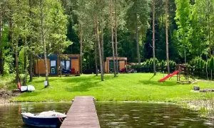 Idealne miejsce na wakacje w Polsce: drewniane domki, jezioro z łódką i plac zabaw dla dzieci.