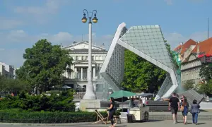 Plac Wolności tętni życiem. Ludzie spacerują obok nowoczesnej fontanny i lodziarni, ciesząc się słonecznym dniem.