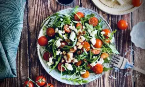 Frischer Rucola Salat mit Kirschtomaten, Feta und Croutons auf rustikalem Holztisch.