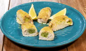 Involtini di pesce spada ripieni di erbe aromatiche, dorati e serviti su un piatto blu con spicchi di limone.