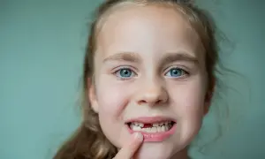 Uśmiechnięta dziewczynka z niebieskimi oczami pokazuje lukę po wypadniętym mleczaku. To znak, że czas na nowe zęby!