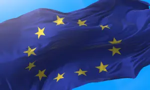 Flaga Unii Europejskiej falująca na wietrze na tle błękitnego nieba.
