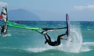 Windsurfer wykonuje akrobację na turkusowej wodzie, tworząc fontannę rozprysków.