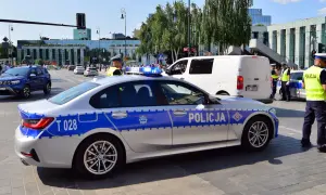 Radiowóz policyjny z włączonymi sygnałami świetlnymi na ulicy, obok policjanci.
