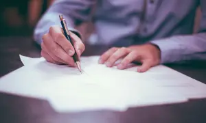 Ręka pisze na dokumencie, zastanawiając się, jaki podatek od spadku po wujku będzie należny.