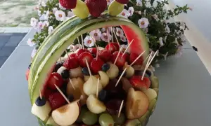 Koszyk z arbuza wypełniony owocami: truskawkami, winogronami, melonem i śliwkami. Idealne owoce na wesele, ozdobione malinami i borówkami.