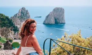 Donna sorridente con vista sui Faraglioni e il mare azzurro, un ricordo dalla spiaggia di Marina Piccola.
