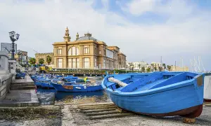 Barche blu nel porto del capoluogo della Puglia, con un edificio storico sullo sfondo.