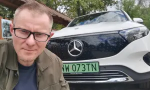 Mężczyzna w okularach pozuje do selfie na tle białego Mercedesa EQB.