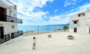 Bambino ammira il mare azzurro dalla piazzetta Petrone a Vieste, con case bianche e cielo nuvoloso.