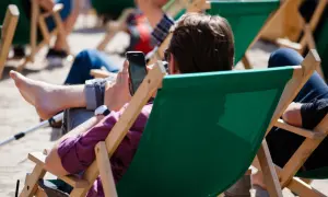 Mężczyzna w okularach przeciwsłonecznych relaksuje się na leżaku, przeglądając telefon. Idealny urlop wypoczynkowy.