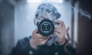 Osoba w kapturze śledzi i fotografuje gwiazdy przez obiektyw aparatu, otoczona mgiełką dymu.