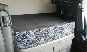 L'intérieur d'un camion Scania, prêt pour la nuit. Le lit est fait, avec une housse au motif abstrait gris et noir, parfait pour le scania tuning nuit.