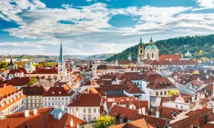 Dachlandschaft von Mala Strana in Prag mit roten Ziegeldächern und Kirchtürmen unter einem blauen Himmel mit Wolken.