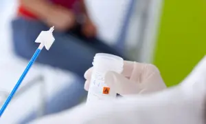 Ręka w rękawiczce trzyma pojemnik z płynem do cytologii. Obok leży szczoteczka do pobierania wymazu.