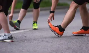 Atleti si preparano per la gara di corsa, allungando le gambe e indossando scarpe sportive colorate.