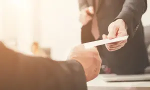 Dwaj mężczyźni w garniturach wymieniają dokumenty. Jeden z nich, prawdopodobnie najemca, wręcza coś drugiemu.