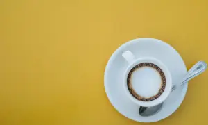 En vit kopp med kaffe macchiato står på en tefat med en sked. En perfekt start på dagen, det är vad macchiato betyder.
