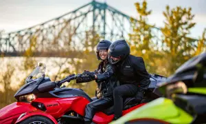 Para jadąca na czerwonym Can-Am Spyder, w tle most i jesienne drzewa.