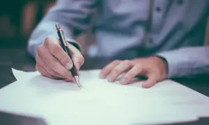 Dłoń pisze długopisem na dokumencie. Może to być umowa, faktura, a nawet wypełnianie wniosku o nip-8.