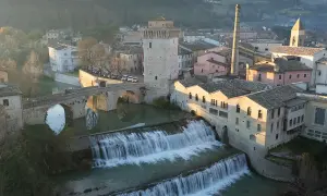 Cascata e ponte ad arco a Fermignano, vicino Urbino, con edifici storici e una ciminiera.