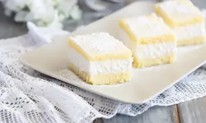 Tre soffici fette di torta Kinder Paradiso, cosparse di zucchero a velo, su un piatto bianco.