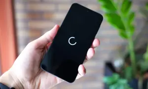 Dłoń trzyma czarny smartfon z białym kółkiem ładowania na ekranie.