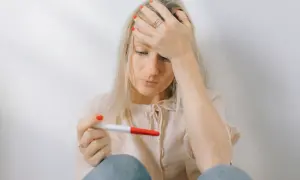 En kvinna med blont hår håller ett graviditetstest och ser bekymrad ut. Hon har handen mot pannan, kanske en tanke på abort vecka 6.
